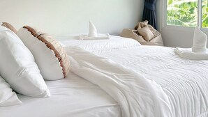 A neatly made bed with white linens and pillows, a window with a view of greenery, and a dark curtain. - BAOBAB (Patong)