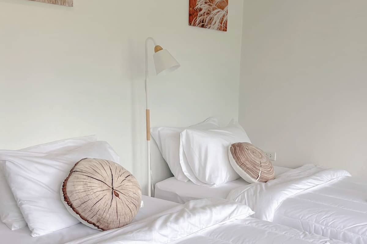 Une chambre avec deux lits, du linge de lit blanc et une lampe de chevet.