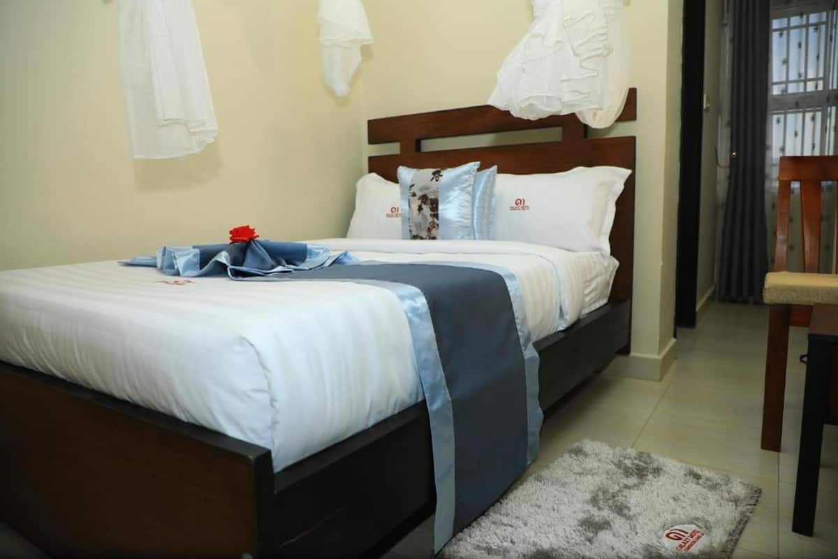Una cama bien hecha con colcha azul y blanca, un cabecero de madera y una alfombra gris en el suelo.