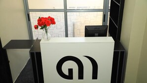 Un mostrador de recepción con un logotipo, un jarrón de flores rojas y un monitor de computadora.