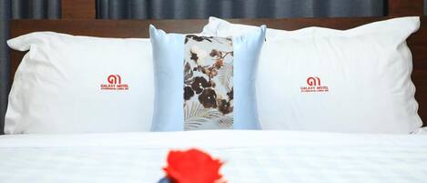 A neatly made bed with white bedding and two pillows featuring a floral design and the Galaxy Motel logo.