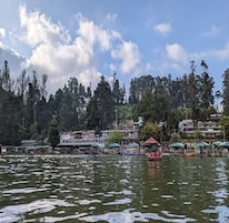 A lakeside view with boats, a dock, and buildings in the background.