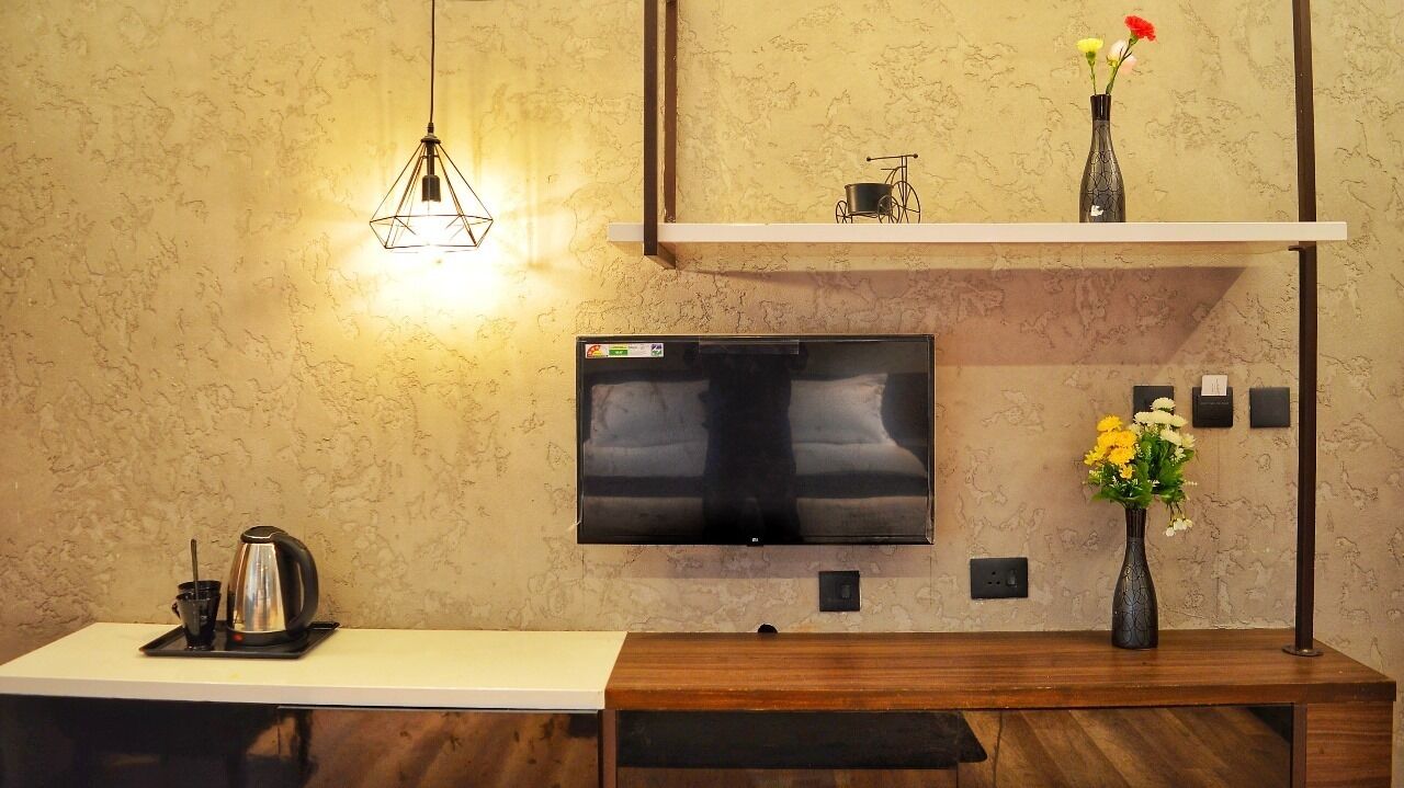 A modern kitchen with a flat-screen TV mounted on the wall, a wooden bench, a coffee station, and a vase with flowers on a shelf.