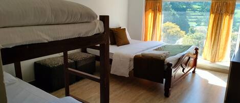 A room with bunk beds, a bed, and a window with curtains.