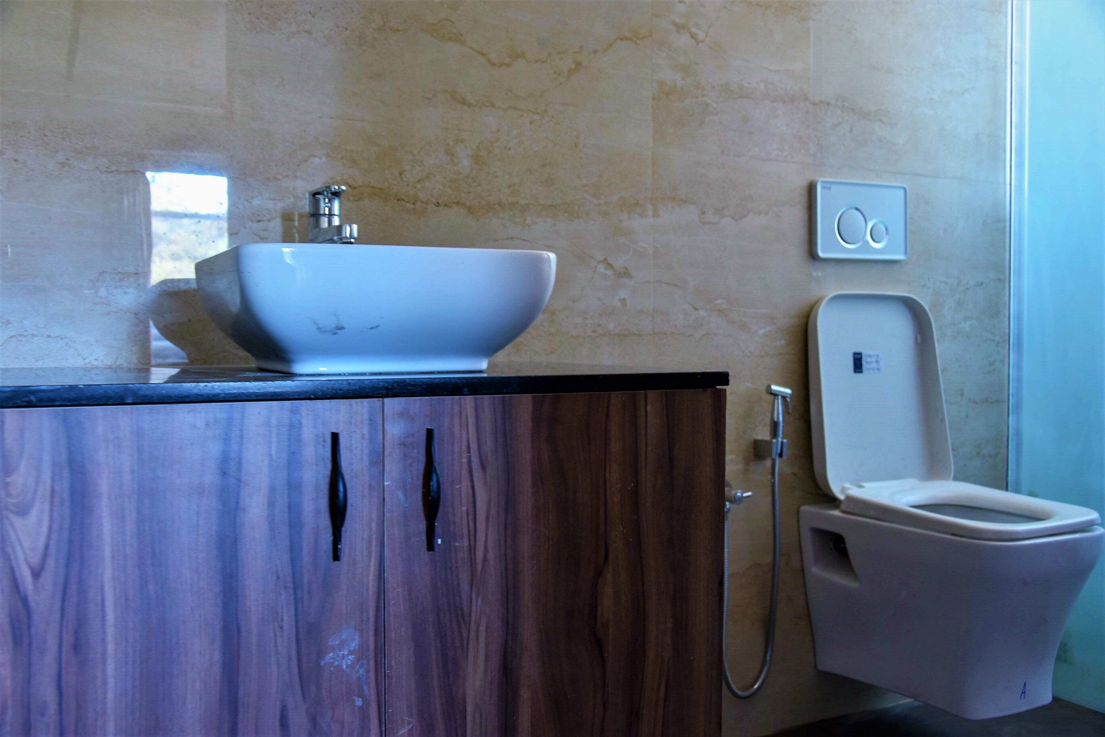 A bathroom with a wooden cabinet, a white sink, and a toilet with a shower attachment.