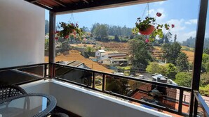 Un balcon donnant sur un paysage rural, une table en osier et des jardinières suspendues.