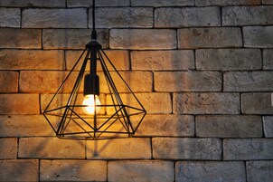 A geometric metal light fixture with a visible bulb against a brick wall.