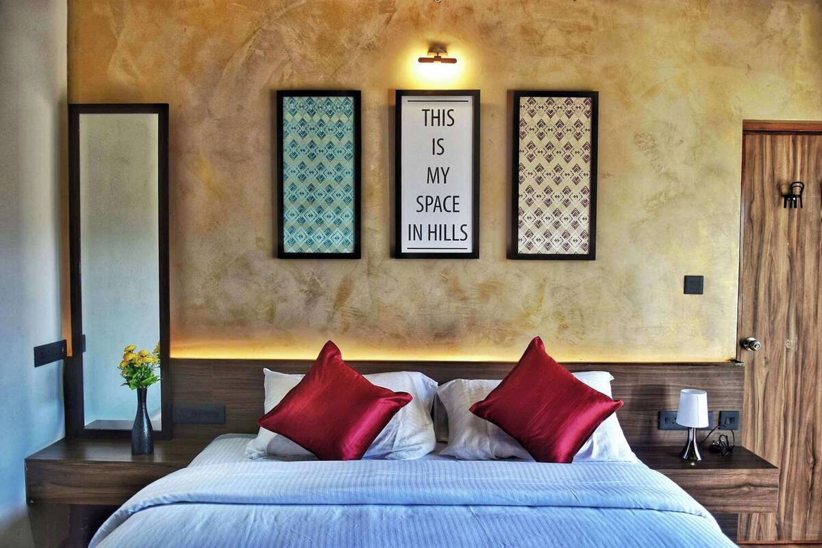 A bedroom with a bed, two red pillows, a nightstand with a lamp, and three framed signs on the wall.