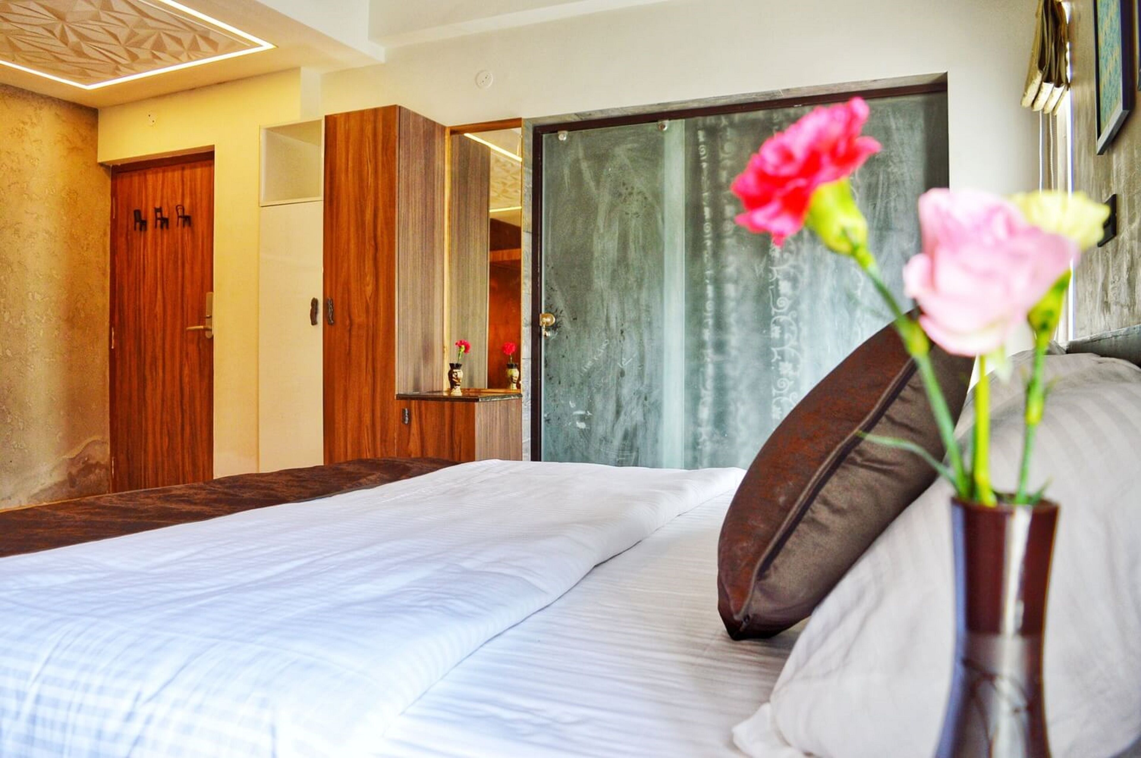 A hotel room with a large bed, a wooden wardrobe, a mirror, and a vase with flowers.