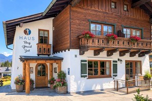 Ein Holzbau mit einem Schild, auf dem 'HAUS Berg Gesund Zelt' steht, und einem Balkon mit Blumenkästen.