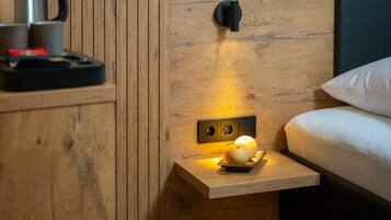 Een kleine hotelkamer met een wand van houten panelen, een nachtkastje met een lamp, een waterkoker en een bord met twee appels.
