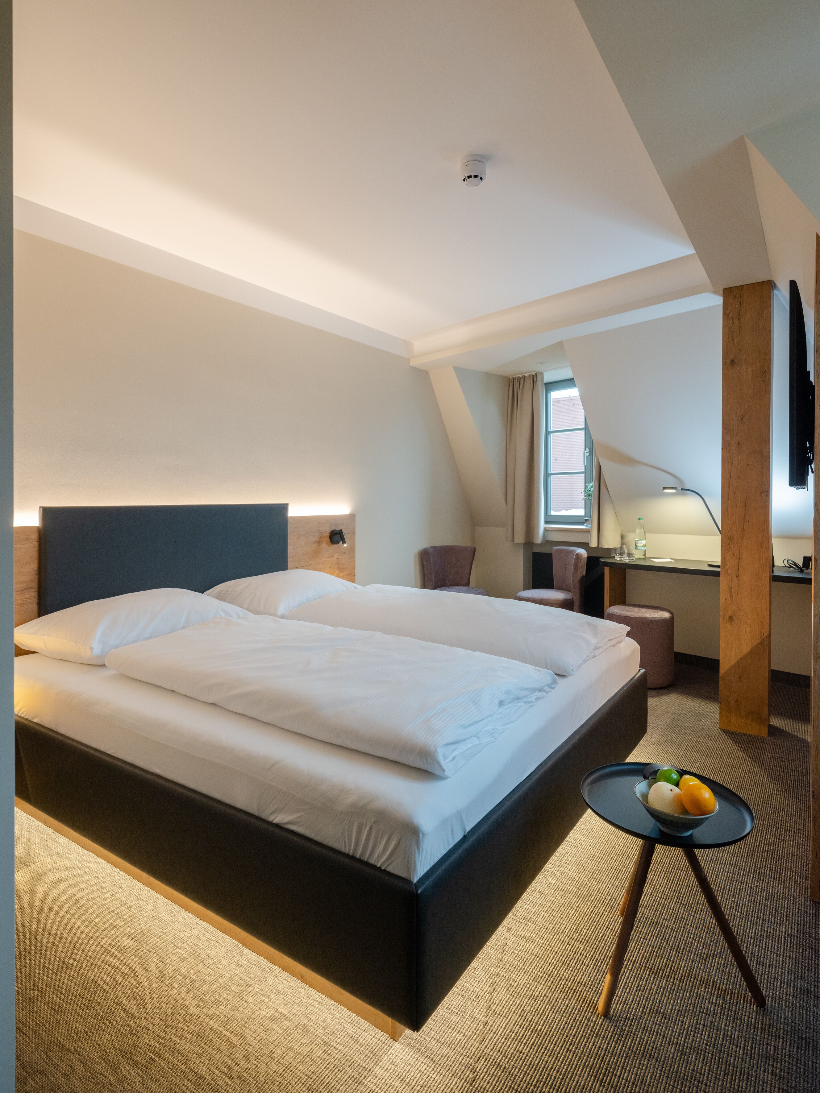 Una habitación de hotel moderna con una cama grande, un escritorio y una mesita redonda con fruta.
