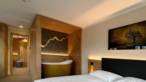 Ett hotellrum med en stor säng, en väggpanel i trä, ett runt badkar och en tavla som föreställer ett träd.