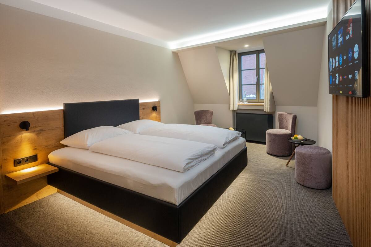 A modern hotel room with a large bed, a desk, a chair, and a TV mounted on the wall.