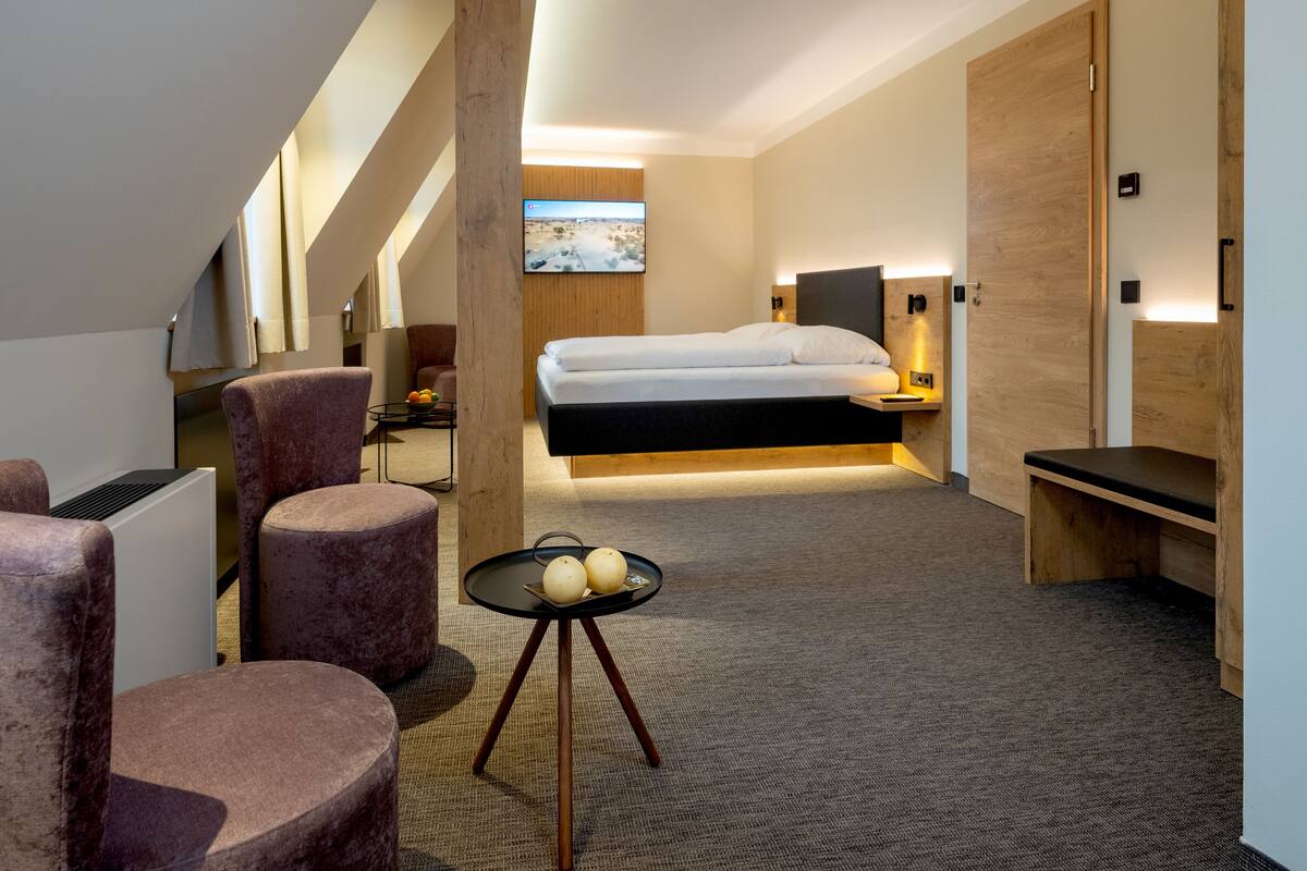 A modern hotel room with a bed, a desk, a chair, and a TV.