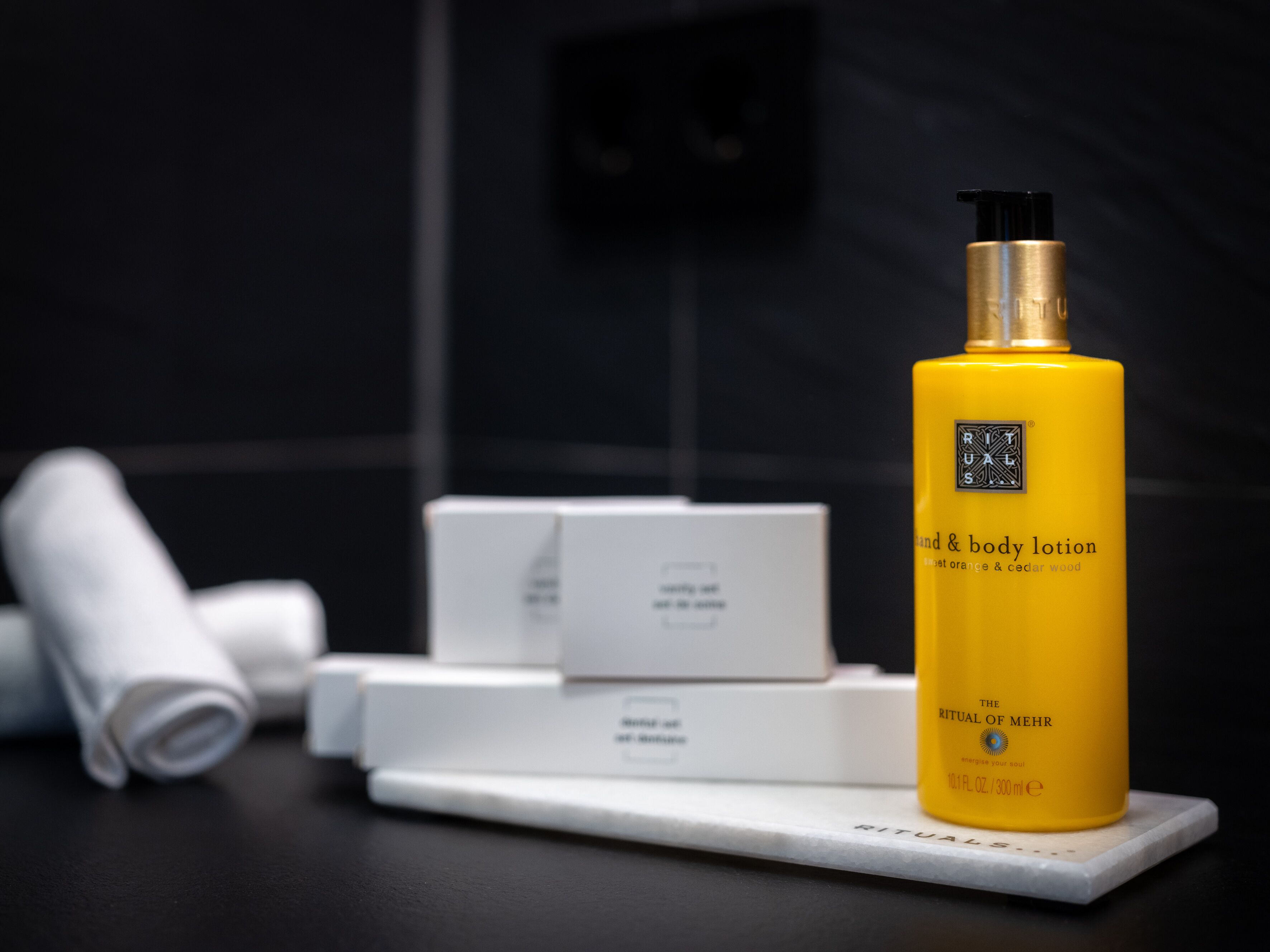 A bathroom with a yellow bottle of lotion, white boxes, and a white towel on a marble countertop.