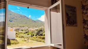 Una ventana abierta con vistas a un paisaje montañoso, un cartel en la pared y una cortina.