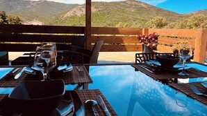 Un área de comedor al aire libre con mesas y sillas, una pérgola de madera y vistas a montañas.