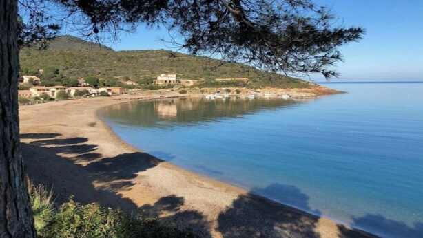 Un paisaje costero con una playa arenosa, mar tranquilo y una pequeña construcción en una colina.