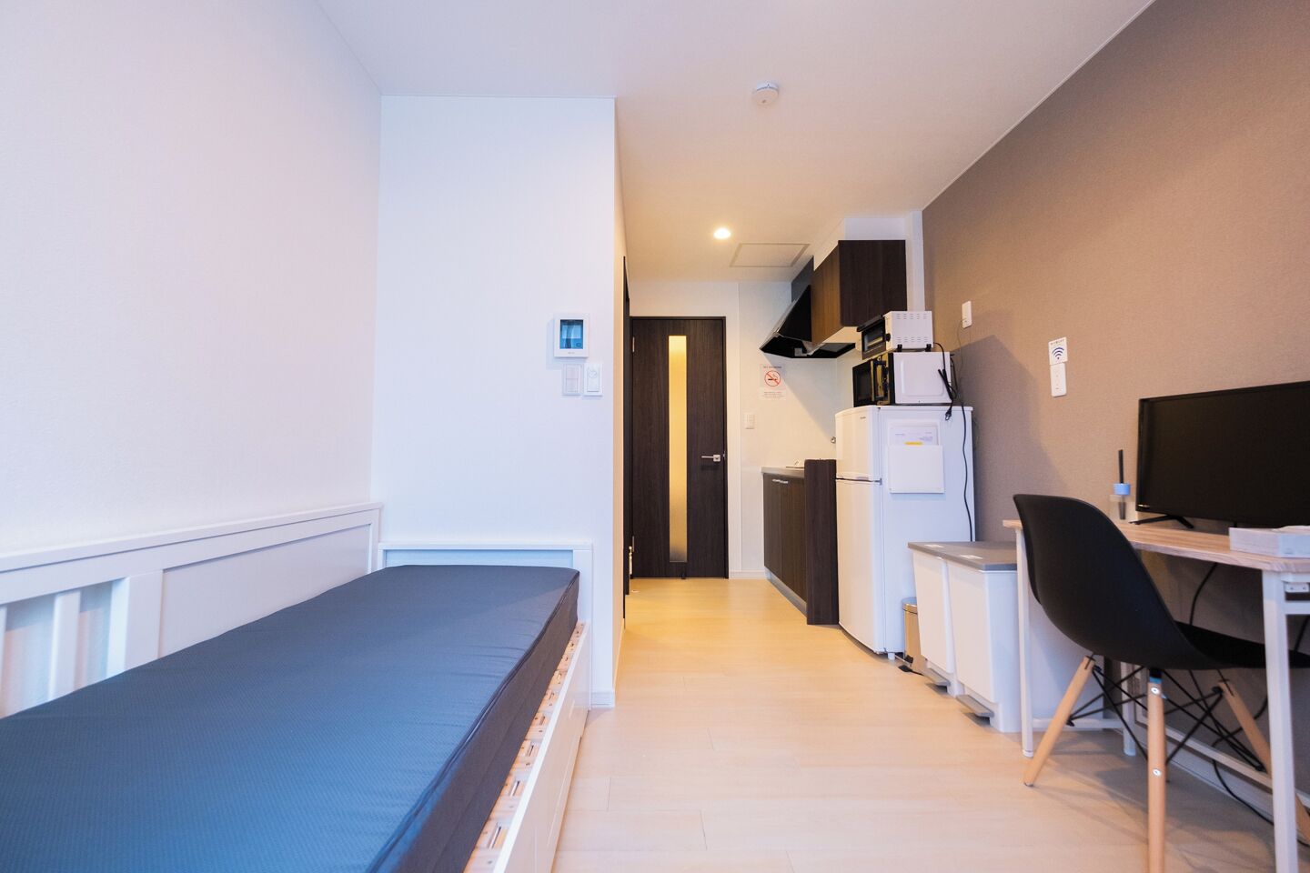 A compact room with a bed, a desk, a chair, a refrigerator, and a microwave.