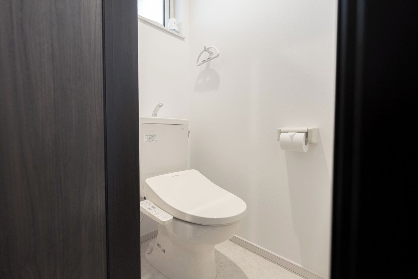 Un baño pequeño y moderno con inodoro, ducha y un dispensador de papel higiénico en la pared.