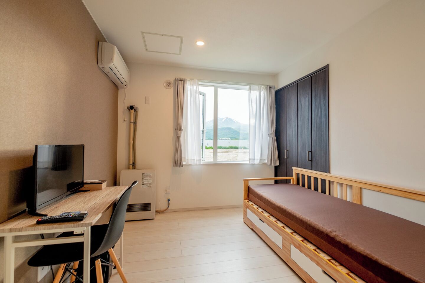 A small room with a bed, a desk with a TV, and a window with curtains.