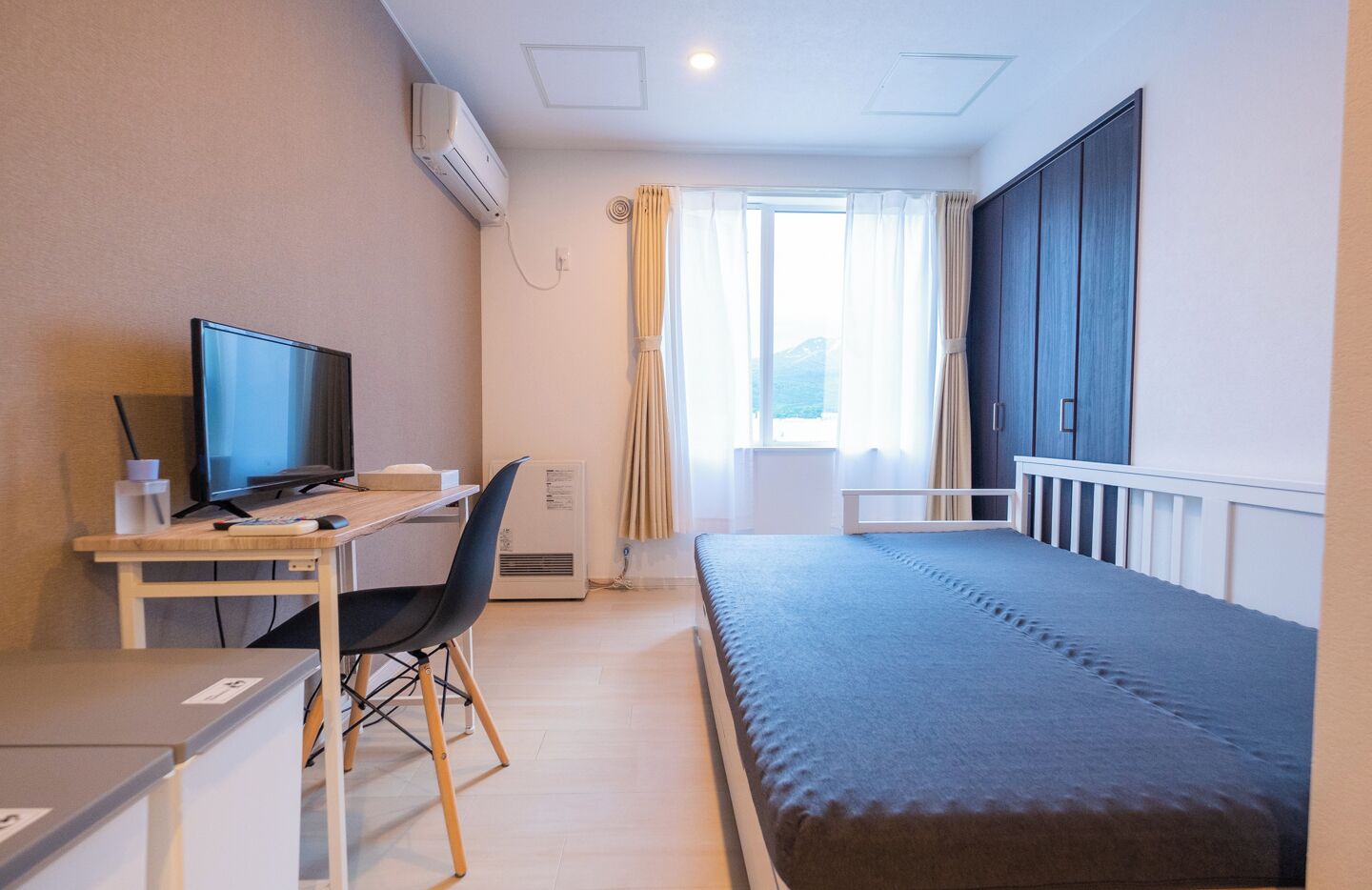 A hotel room with a bed, a desk with a computer, a chair, and a window with curtains.