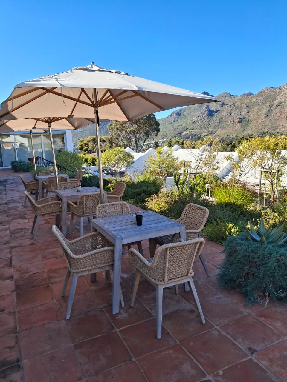 Patio esterno con mobili in vimini e un ombrellone grande, con vista su un paesaggio montuoso.