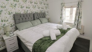 En pænt redt seng med et grønt plaide, en senget lampe og et natbord med skuffer.