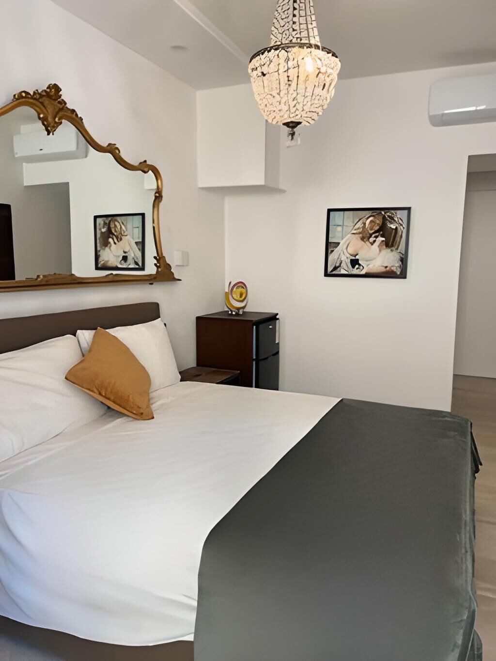 Une chambre à coucher avec un grand lit, un lustre, un miroir et deux tableaux encadrés accrochés au mur.
