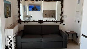 Un saló modern amb un sofà fosc, un mirall gran i ornamentat, i un ventilador de sostre.