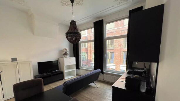Una sala de estar moderna con una mesa de comedor negra, un sofá, un televisor y un ventanal con vistas a edificios.