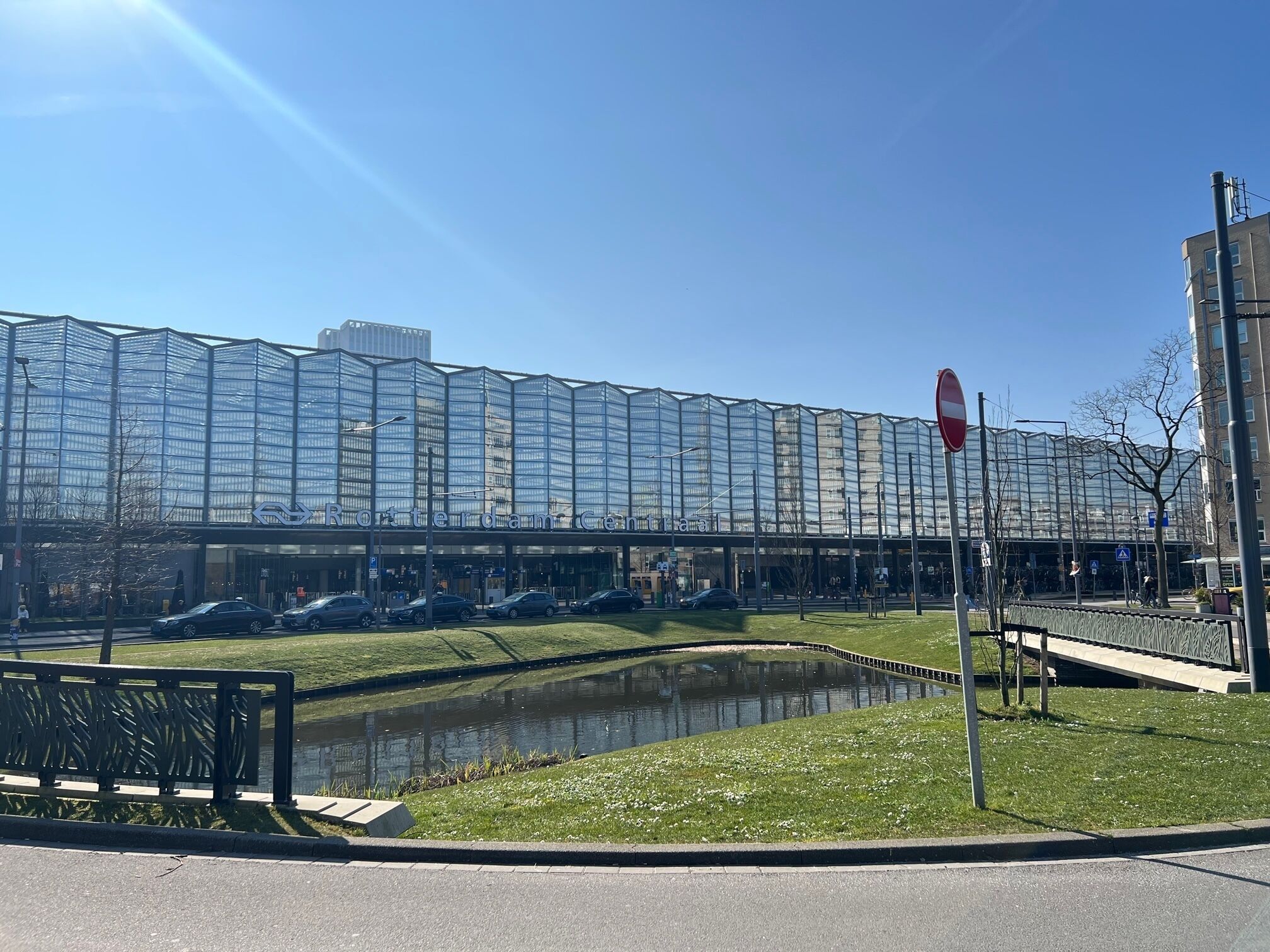 Un edificio moderno con fachada de vidrio, un pequeño estanque y un paseo peatonal.