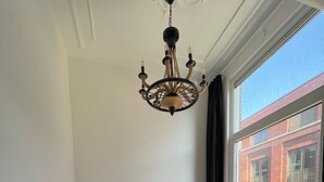 Una habitación con dos camas junto a una pared, una ventana que da a un edificio de ladrillo y una araña.