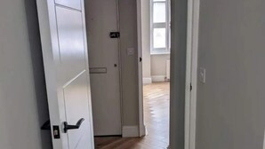 Un couloir doté d’un plancher en bois et de murs blancs, qui mène à une pièce avec une porte et une fenêtre.