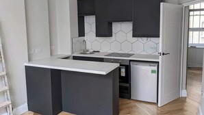 Une cuisine de taille réduite, avec des meubles de couleur sombre, un plan de travail blanc et un lave-vaisselle.