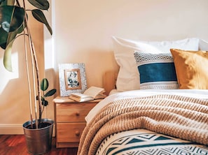 A bedroom with a bed, pillows, a bedside table, a framed picture, a potted plant, and a knitted blanket. - TurnKey | City Mall Studio (Praha)