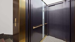A modern elevator with a metallic finish, a handrail, and a control panel.