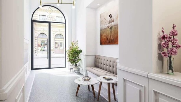 A hallway with a bench, two round tables, a hanging light fixture, and a door leading to a shop.