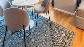 A modern living room with a round dining table, grey chairs, a blue patterned rug, a hanging light fixture, and a framed artwork on the wall. - TurnKey | Angelo Roma Studio I (Praha 2)