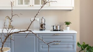 A kitchen with white cabinets, a coffee maker, a pot, and a potted plant. - TurnKey | Angelo Roma Studio I (Praha 2)