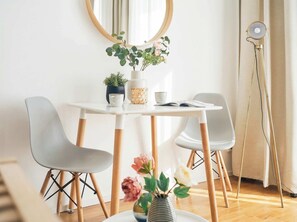 A dining area with a white table, two grey chairs, a potted plant, a vase with flowers, and a floor lamp.
