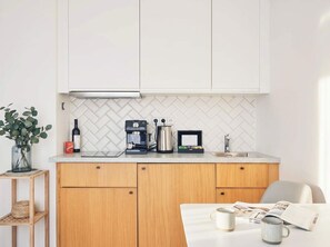 A kitchen with white cabinets, a herringbone tile backsplash, and a countertop with a coffee maker, kettle, and toaster.