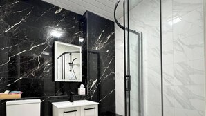 Un bagno moderno con cabina doccia in vetro curvo, vaso bianco e mobile lavabo bianco con dettagli in marmo nero.