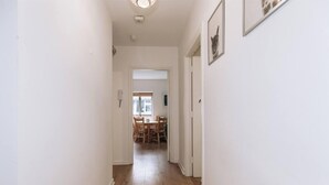 Un corridoio stretto con pavimento in legno, pareti bianche e una porta che dà su una sala da pranzo con mobili in legno.