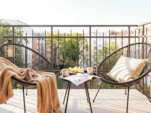 A balcony with two wicker chairs, a small table with a cup, a plate of fruit, and a blanket. - TurnKey | King George Studio with Balcony II (Praha 3)