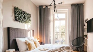 Un dormitorio con cama, mesita de noche, lámpara, cortinas y vistas al exterior.
