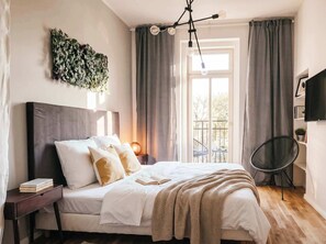 A bedroom with a bed, bedside table, lamp, curtains, and a view of the outdoors. - TurnKey | King George Studio with Balcony II (Praha 3)