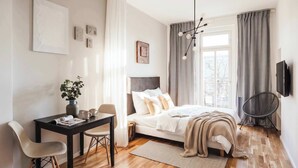 A modern bedroom with a bed, bedside table, chair, and a desk with a plant.