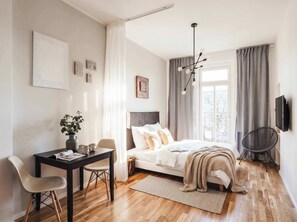 A modern bedroom with a bed, bedside table, chair, and a desk with a plant.